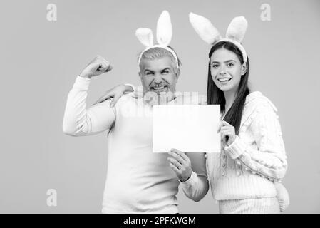 Le couple de Pâques vêtu de costume tenant un tableau blanc vierge pour votre texte. Couple de lapin de Pâques isolé sur fond bleu. Banque D'Images