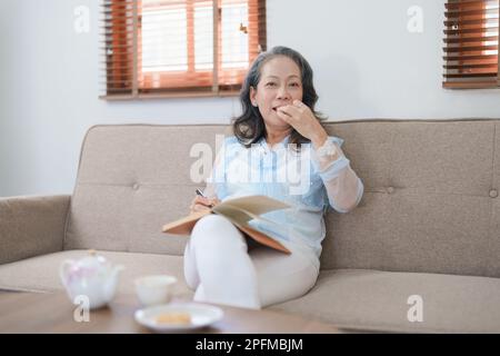 Portrait d'une femme asiatique âgée tenant un carnet à manger des collations et à boire du thé. Banque D'Images