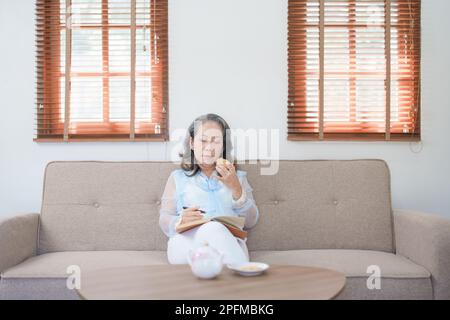 Portrait d'une femme asiatique âgée tenant un carnet à manger des collations et à boire du thé. Banque D'Images