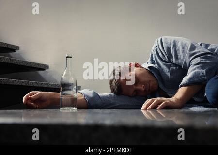 Homme accro avec boisson alcoolisée dormant au sol à l'intérieur Banque D'Images