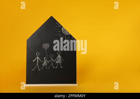 Dessin au craie de parents avec leurs enfants sur un tableau noir en forme de maison sur fond orange, espace pour le texte. Jour de la famille Banque D'Images