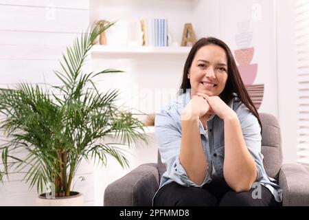 Belle femme en surpoids assise dans un fauteuil à la maison Banque D'Images