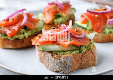 Délicieux sandwichs avec saumon, avocat, concombre et oignon sur l'assiette, en gros plan Banque D'Images