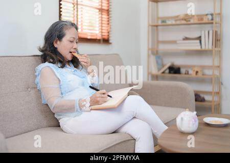 Portrait d'une femme asiatique âgée tenant un carnet à manger des collations et à boire du thé. Banque D'Images