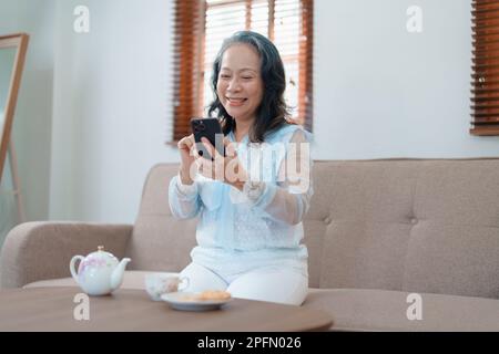 Portrait d'une femme asiatique âgée tenant un téléphone portable avec des en-cas et du thé. Banque D'Images