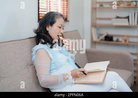 Portrait d'une femme asiatique âgée tenant un carnet à manger des collations et à boire du thé. Banque D'Images