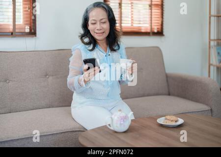Portrait d'une femme asiatique âgée tenant un téléphone portable avec des en-cas et du thé. Banque D'Images