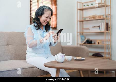 Portrait d'une femme asiatique âgée tenant un téléphone portable avec des en-cas et du thé. Banque D'Images
