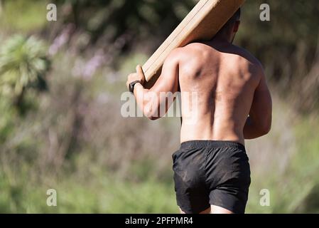 Homme portant une bûche de bois dans un test de la course. Coureurs de boue, course d'obstacles extrêmes Banque D'Images