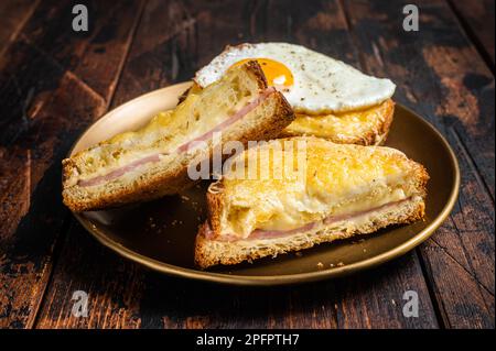 Toasts français croque monsieur et croque madame, sandwichs grillés sur pain de brioches avec tranches de jambon, fromage emmental fondu et œuf.Arrière-plan en bois Banque D'Images