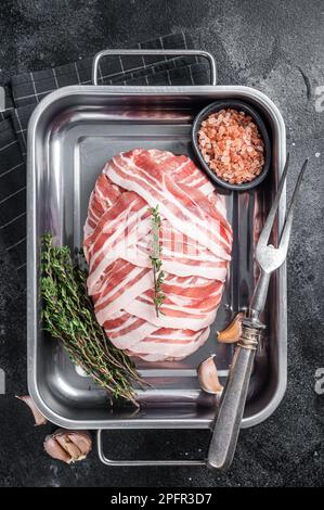 Cuisson du pain de viande cru avec de la viande de bœuf hachée et du bacon dans un plateau en acier, pain de viande frais. Arrière-plan noir. Vue de dessus. Banque D'Images