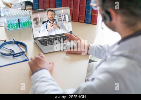 Un médecin s'assoit dans son bureau médical et mène une consultation virtuelle avec un collègue à l'aide d'un ordinateur portable. Les médecins discutent du medi d'un patient Banque D'Images