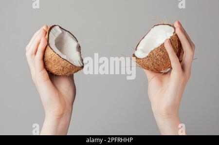 Mains tenant la noix de coco fendue fissurée, deux moitiés de fruits de noix de coco. Banque D'Images