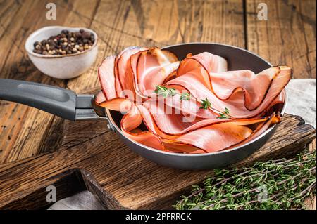 Tranches minces de bacon de jambon de la Forêt-Noire allemande dans une poêle. Arrière-plan en bois. Vue de dessus. Banque D'Images