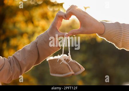 L'homme et la femme enceinte font des gestes cardiaques avec les mains et tiennent des chaussures chaudes pour bébé sur fond d'automne nature. Futurs parents attendant le bébé. Le concept de la Fête des mères et de la Journée des femmes Banque D'Images