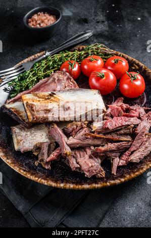 Côtelettes de bœuf fumées et grillées dans une assiette rustique aux herbes. Arrière-plan noir. Vue de dessus. Banque D'Images