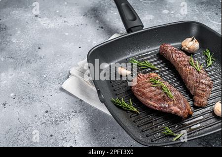 Rôti sur une poêle à frire à rabat ou sur une viande de bœuf Bavette au romarin. Arrière-plan gris. Vue de dessus. Copier l'espace. Banque D'Images