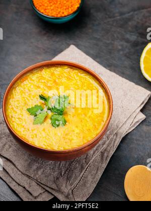 Soupe indienne de lentilles rouges sur fond sombre. Bol de soupe aux lentilles, ingrédients et cuillère en bois. Gros plan Banque D'Images