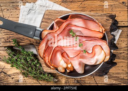 Tranches minces de bacon de jambon de la Forêt-Noire allemande dans une poêle. Arrière-plan en bois. Vue de dessus. Banque D'Images