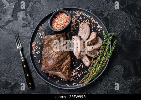 Griller un steak de bœuf Wagyu vieilli tri Tip sur une assiette de sel rose. Arrière-plan noir. Vue de dessus. Banque D'Images