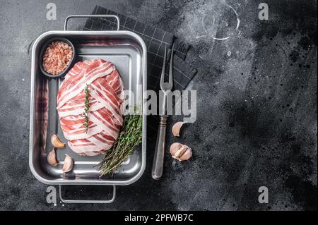 Cuisson du pain de viande cru avec de la viande de bœuf hachée et du bacon dans un plateau en acier, pain de viande frais. Arrière-plan noir. Vue de dessus. Copier l'espace. Banque D'Images