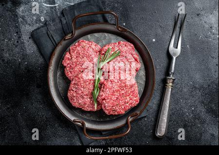Frikadellen non cuite de viande de bœuf hachée, côtelettes de viande crue. Arrière-plan noir. Vue de dessus. Banque D'Images
