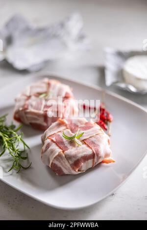 Préparation des wraps de fromage en les enveloppant dans une plaque de tranches de bacon avant la cuisson. Banque D'Images