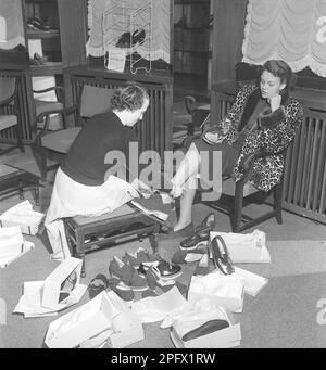 Une jeune femme est bien prise en charge par un commis dans un magasin de chaussures. Le répartiteur essaie différentes chaussures sur les pieds de la dame. Elle a essayé plusieurs paires différentes de chaussures d'été et, à en juger par la photo, elle n'a pas encore trouvé une paire qu'elle pense convenir. Suède 1949 Kristoffersson réf. AU10-10 Banque D'Images