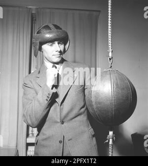 Un jeune homme en costume se tient avec sa garde vers le haut. Il a l'intention de frapper une boule de repère qui est attachée au sol et au plafond, également appelée boule sol-plafond. Sans gants et avec seulement une protection de la tête pendant son entraînement, il est mal équipé pour la tâche. Suède 1943. Kristoffersson réf. B22-4 Banque D'Images