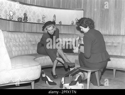 Une jeune femme est bien prise en charge par un commis dans un magasin de chaussures. Le répartiteur essaie différentes chaussures sur les pieds de la dame. Elle a essayé plusieurs paires différentes de chaussures d'été et, à en juger par la photo, elle n'a pas encore trouvé une paire qu'elle pense convenir. Suède 1948 Kristoffersson réf. AO1-5 Banque D'Images