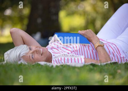 Senior woman reading book posé sur l'herbe Banque D'Images