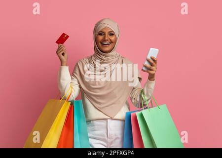 Bonne femme musulmane dans hijab tenant un smartphone, une carte de Creadit et des sacs de shopping Banque D'Images