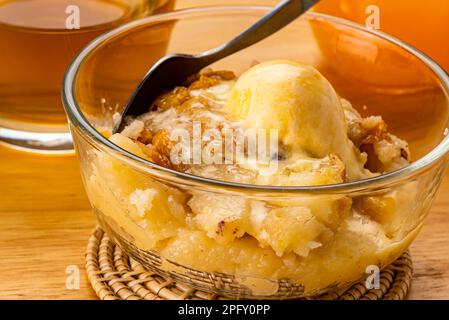 Vue rapprochée de délicieux cobbler à la pêche maison avec une cuillère de glace à la vanille et une cuillère en métal dans un bol en verre transparent sur un tapis en bambou avec un verre Banque D'Images