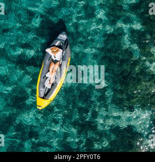 Une femme solitaire dans un chapeau de paille souriant, reposant couché flottant dans un kayak sur les vagues turquoises de la mer Adriatique. Vue aérienne du dessus de la côte. Exotique c Banque D'Images