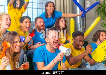 Mélange d'amis amateurs de sport regardant un match de football à la télévision sur un canapé à la maison en applaudisant leurs objectifs d'équipe, en criant exquitamment et en buvant de la bière Banque D'Images