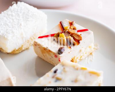 Assiette blanche pleine de différentes pâtisseries. Desserts savoureux avec garniture, noix, flocons de noix de coco. Banque D'Images