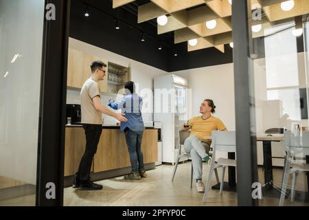 Groupe de jeunes joyeux qui parlent et sourient pendant les pauses-café au bureau. Une équipe de développeurs de logiciels professionnels se détendant dans le Banque D'Images