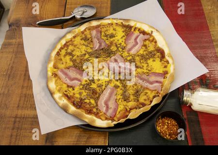 Une merveilleuse pizza à croûte mince moyenne avec du bacon, des viandes variées, du cheddar et du pomodoro sur une table en bois colorée Banque D'Images