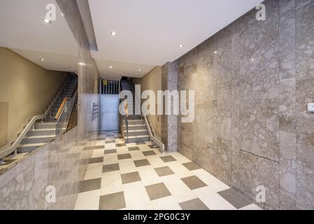 Portail d'un immeuble résidentiel urbain aux murs en marbre, grand miroir intégré au mur et escalier avec ascenseur Banque D'Images