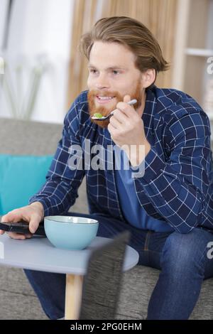 homme mangeant dans un bol tout en regardant la télévision Banque D'Images