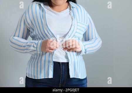 Femme en surpoids essayant de mettre en place une chemise serrée sur fond gris clair, gros plan Banque D'Images