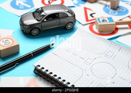 Différents panneaux routiers, carnet avec croquis du rond-point et voiture jouet sur fond bleu clair. École de conduite Banque D'Images