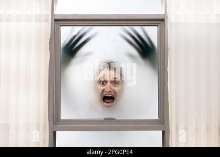 Hurlant homme avec des mains floues a son visage appuyé contre la fenêtre sur un fond brumeux Banque D'Images