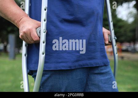 Femme méconnaissable marchant à l'extérieur avec l'aide de béquilles dans le processus de réadaptation physique après une blessure, détail des mains. Banque D'Images