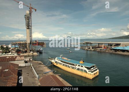 Vue sur la baie de Manado avec le mont Manado Tua en premier plan d'un ferry et d'une partie du pont Soekarno en construction dans la zone côtière de Manado, au nord de Sulawesi, en Indonésie. Banque D'Images