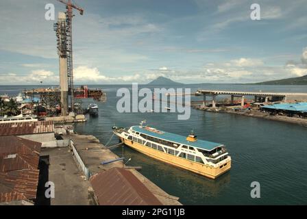 Vue sur la baie de Manado avec le mont Manado Tua en premier plan d'un ferry et d'une partie du pont Soekarno en construction dans la zone côtière de Manado, au nord de Sulawesi, en Indonésie. Banque D'Images