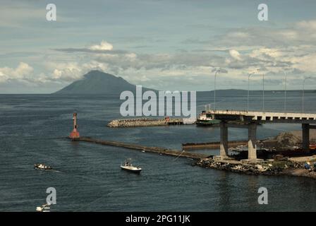 Vue sur la baie de Manado avec le mont Manado Tua au premier plan d'un phare et d'une partie du pont Soekarno en construction dans la zone côtière de Manado, au nord de Sulawesi, en Indonésie. Banque D'Images