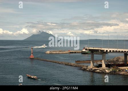 Vue sur la baie de Manado avec le mont Manado Tua au premier plan d'un phare et d'une partie du pont Soekarno en construction dans la zone côtière de Manado, au nord de Sulawesi, en Indonésie. Banque D'Images