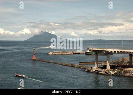 Vue sur la baie de Manado avec le mont Manado Tua au premier plan d'un phare et d'une partie du pont Soekarno en construction dans la zone côtière de Manado, au nord de Sulawesi, en Indonésie. Banque D'Images