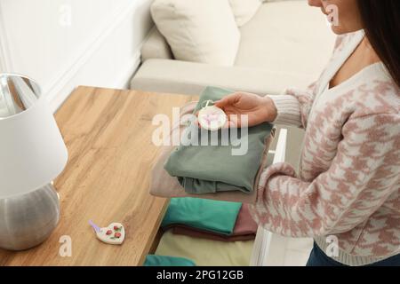 Femme avec des vêtements et un sachet parfumé près de la poitrine des tiroirs à la maison, gros plan Banque D'Images